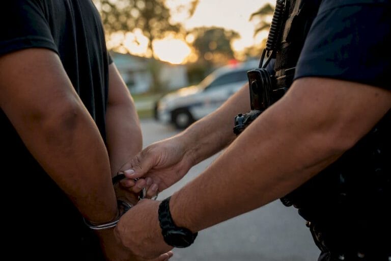 Officer fastening handcuffs at patrol car