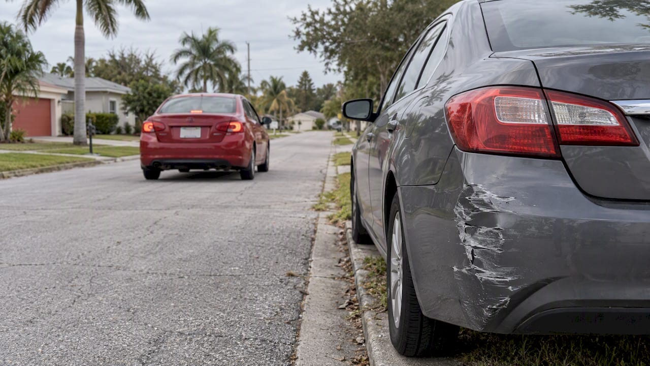 Crimson car leaving a damaged parked sedan